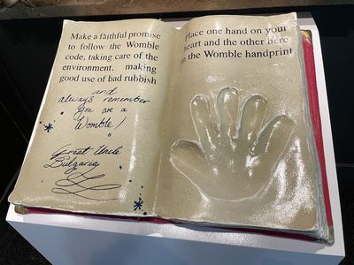 A model of a book saying: 'Make a faithful promise to follow the Womble code, taking care of the environment, making good use of bad rubbish, and always remember you are a Womble! Place one hand on your heart and the other here in the Womble handprint'